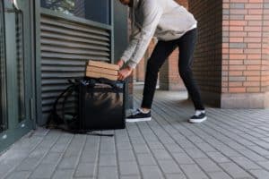 man in grey sweater putting cardboard boxes into black bag for delivery