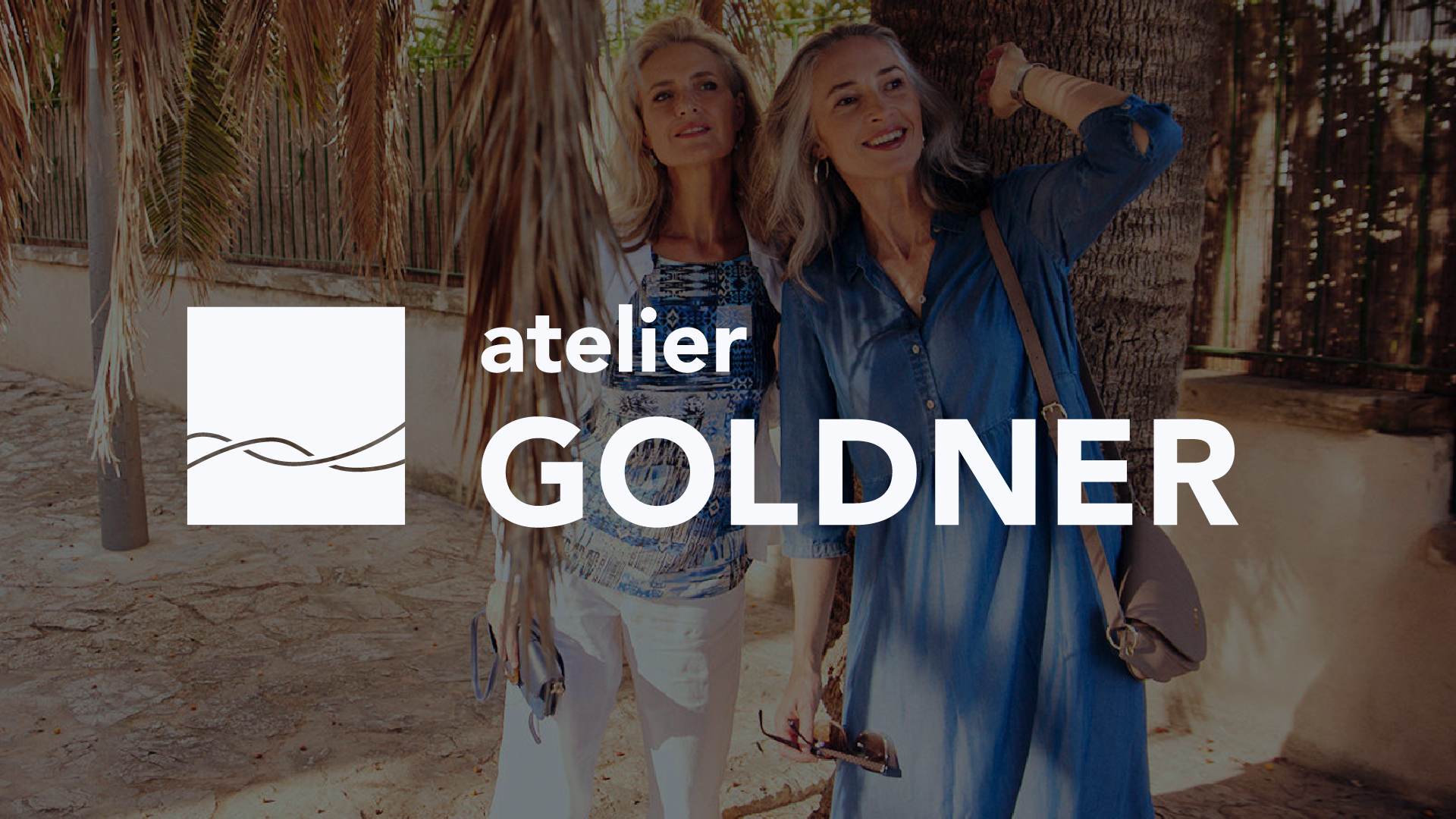 Two stylish older women smiling outdoors with the 'atelier GOLDNER' logo overlaid in white.